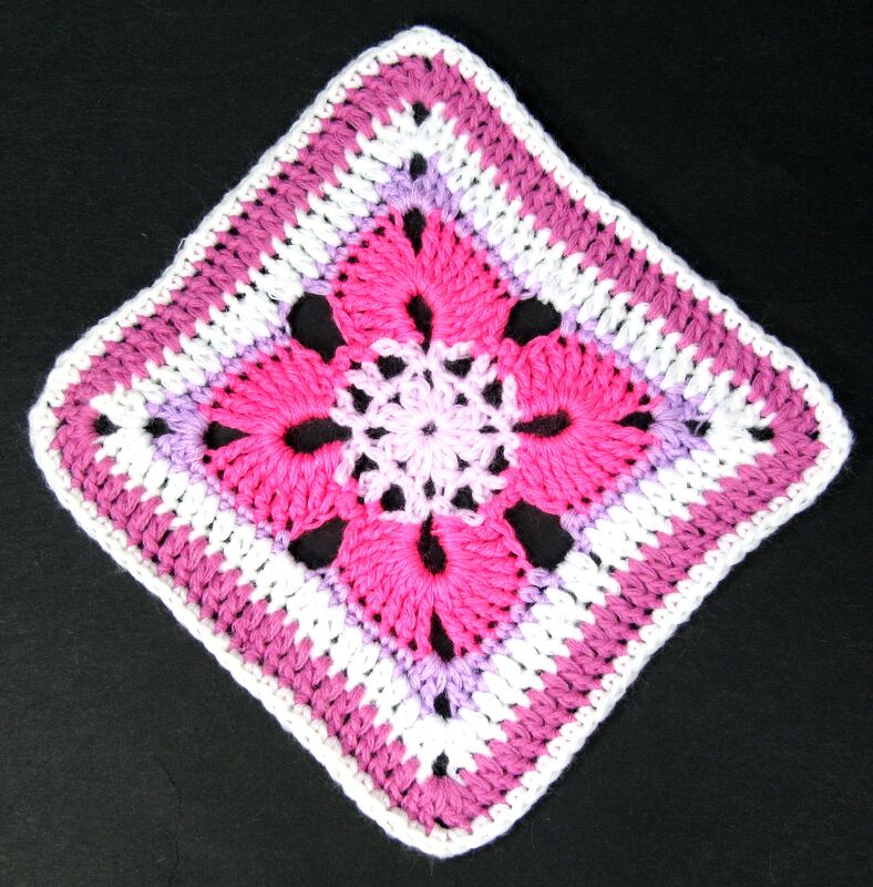 Mehrfarbiges gehäkeltes Quadrat mit zentraler Blüte in Pink, Lila und Weiß auf schwarzem Hintergrund