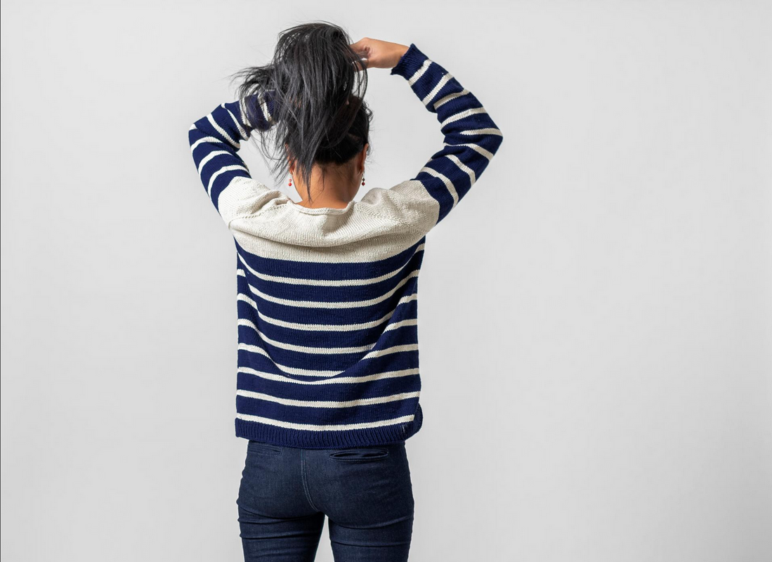 Person von hinten in gestreiftem Strickpullover und Jeans, Haare hochgebunden