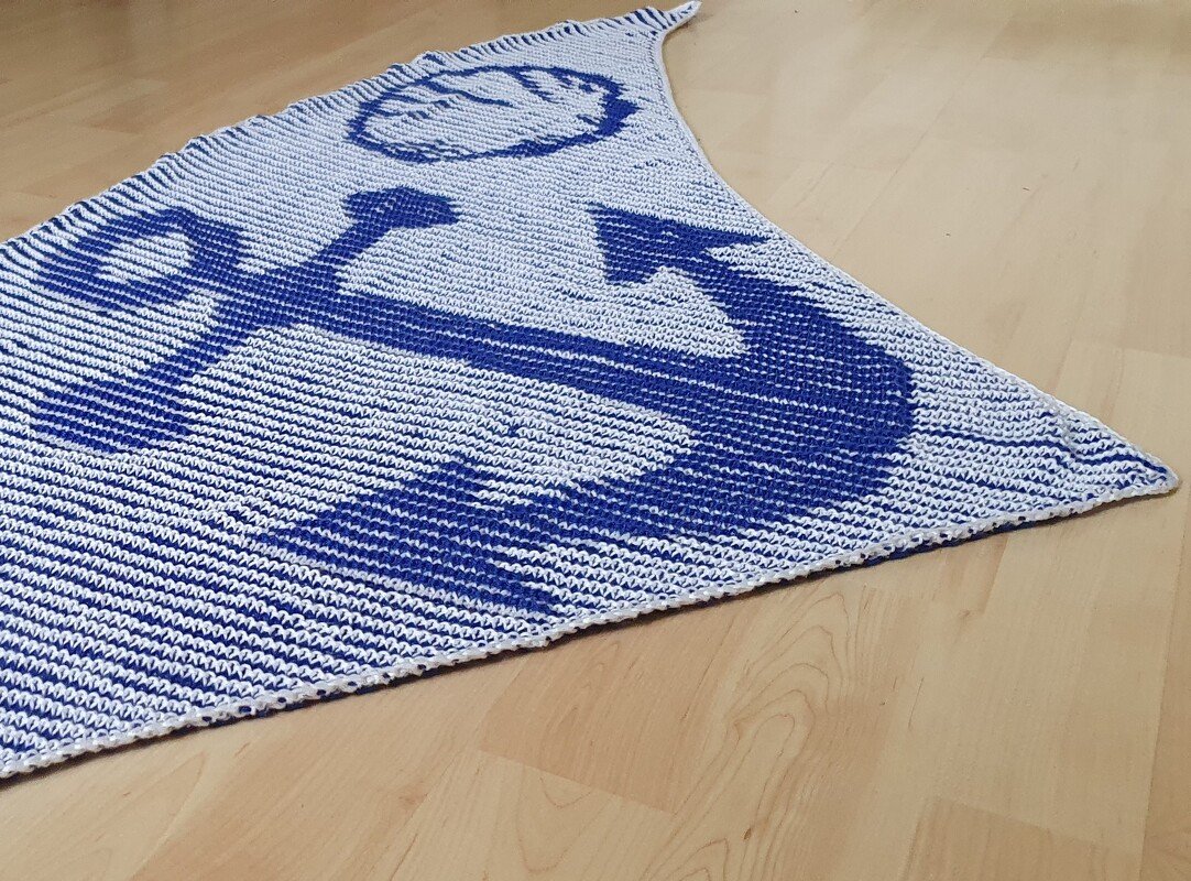 White and blue triangular garter-stitch shawl laid flat showing large blue anchor motif and striped background