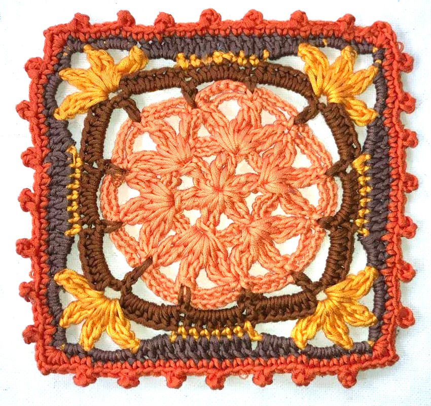 Gehäkeltes quadratisches Motiv mit zentraler Blüte in Orange, braunem Rahmen und gelbem Blattdekor