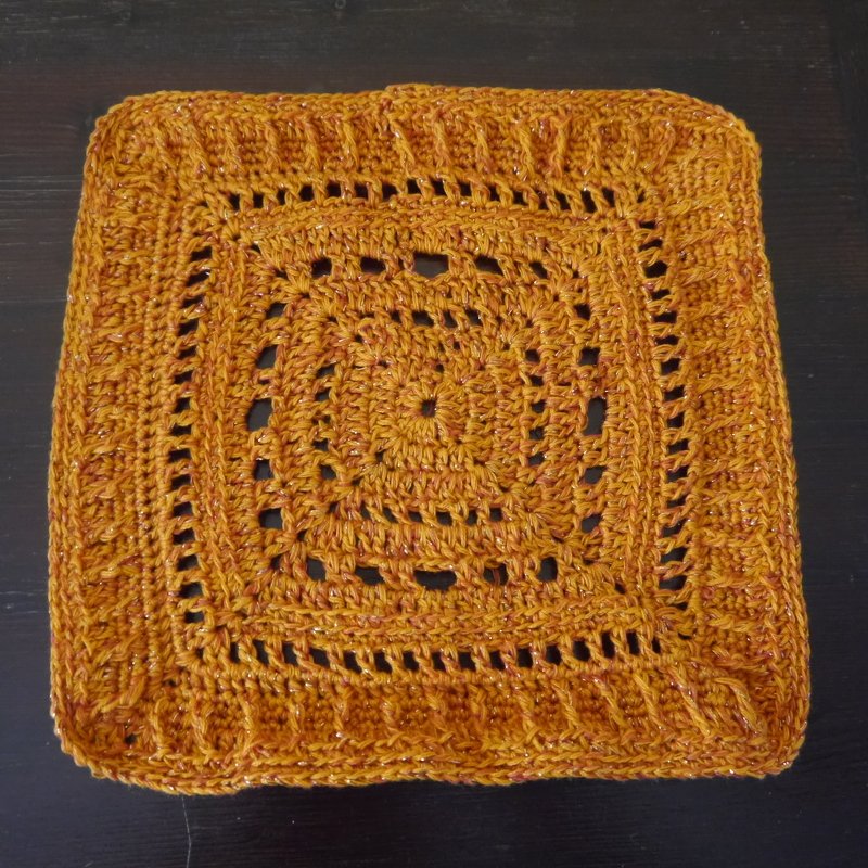 Gehäkeltes Granny-Quadrat in Senfgelb mit schimmerndem Garn und Lochmuster auf dunklem Grund.