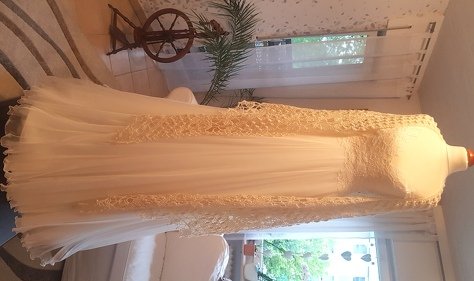 Cream crocheted shawl with openwork pattern draped over a white dress on a mannequin.