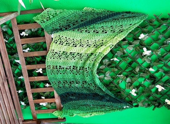 Green ombre crochet shawl with openwork lace draped on a wooden trellis.