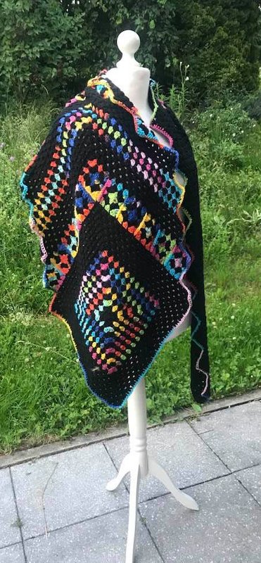 Schwarzer, gehäkelter Schal mit bunten Granny-Squares auf einer Schaufensterpuppe im Garten