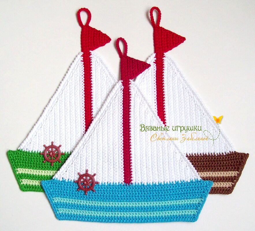 Drei gehäkelte Topflappen in Bootsform mit weißen Segeln, roten Masten und bunten Rümpfen.