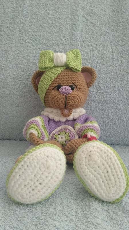 Nahaufnahme gehäkelter Teddybär mit weißen Sohlen, gestreifter Jacke und grüner Stirnschleife