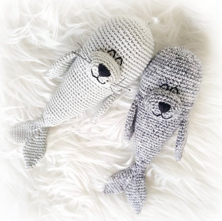 Zwei gehäkelte Amigurumi-Robben in Hell- und Dunkelgrau auf weißem Fell