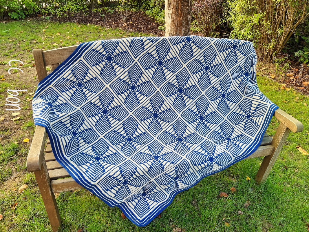 Blue and white crocheted blanket with geometric square pattern on a garden bench
