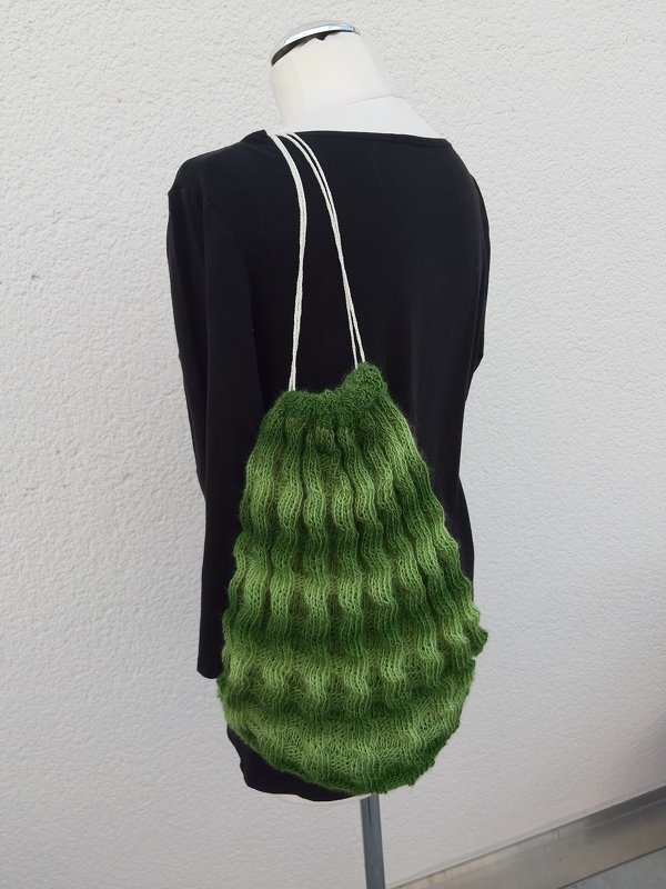 Grüne gestrickte Zugbeuteltasche mit welligem Muster auf einer Schneiderpuppe