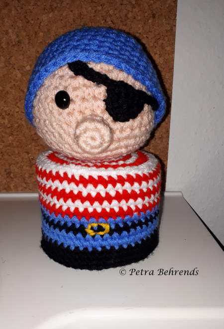 Gehäkelter Pirat als Klorollenhülle mit blauem Bandana, Augenklappe und gestreifter Kleidung.