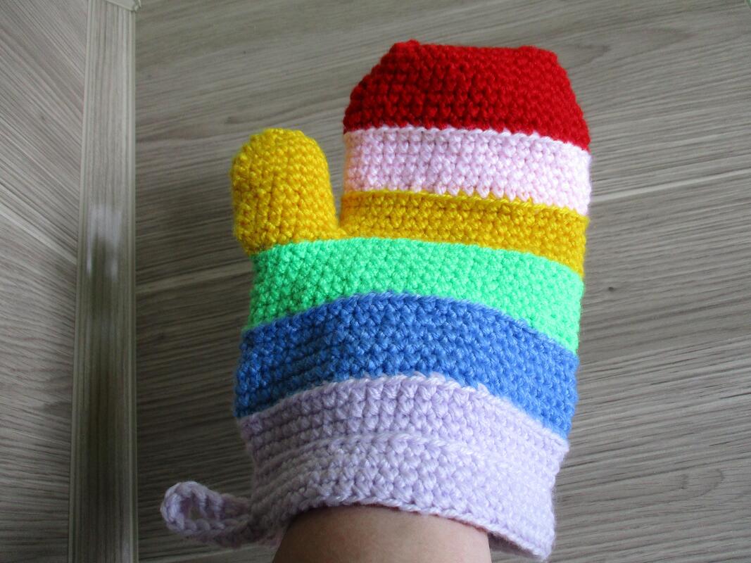 Bunter handgehäkelter Topflappen mit Regenbogenstreifen, an einer Hand getragen vor hellem Holz.