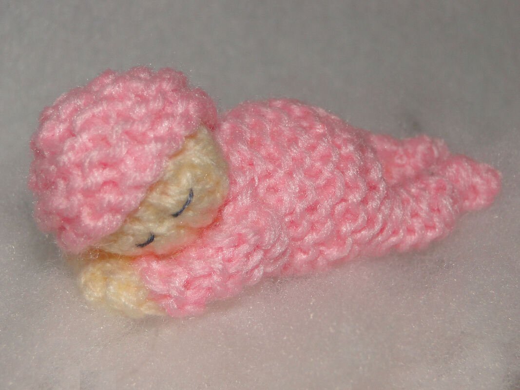 Tiny pink knitted amigurumi baby wrapped in a swaddle