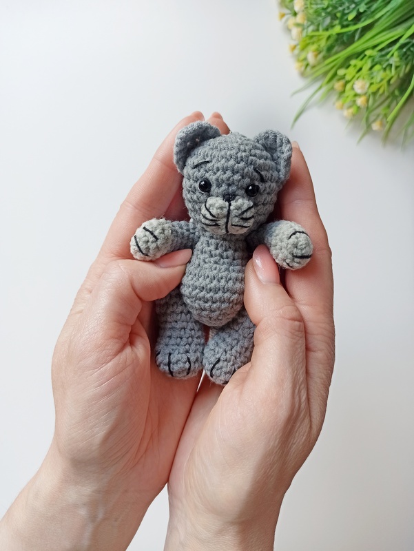 Hands holding a tiny gray crocheted kitten amigurumi with stitched whiskers and black eyes
