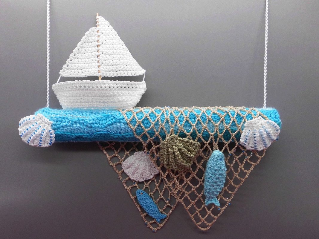 Häkel-Wandbehang mit weißem Segelboot, blau umwickeltem Stab, hängendem Netz und gehäkelten Muscheln und Fischen