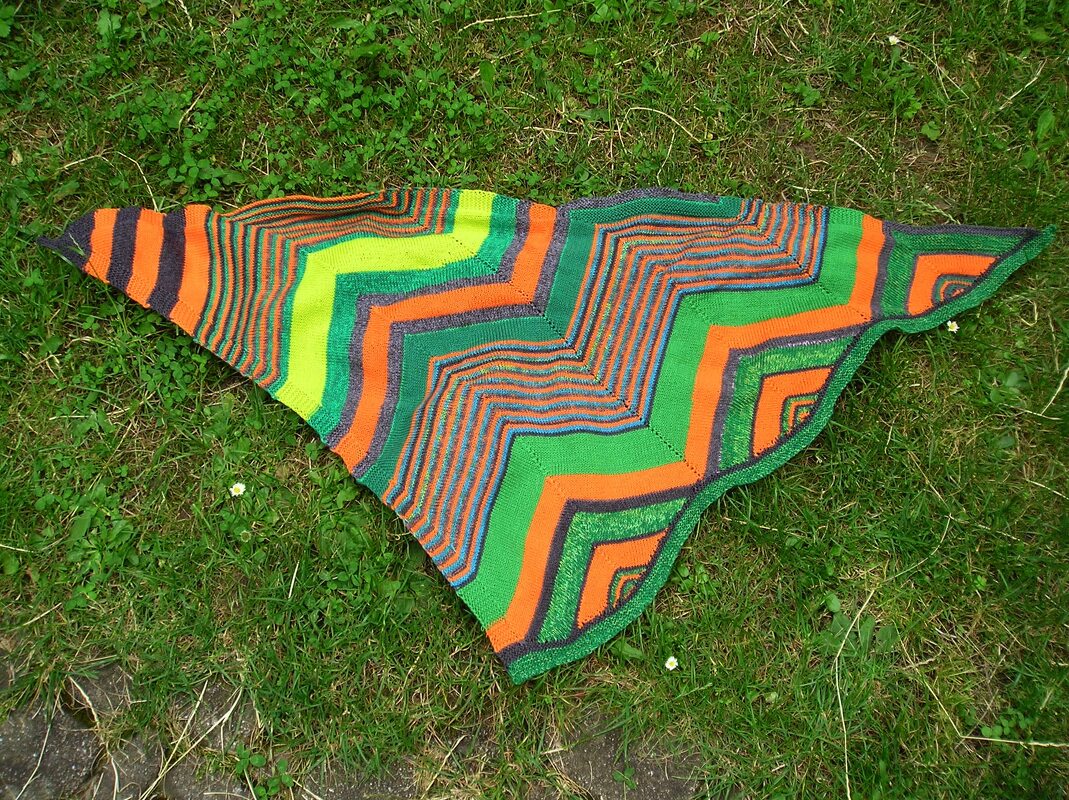 Gestricktes Dreieckstuch mit grünen, orangen und dunklen Zickzackstreifen auf Gras
