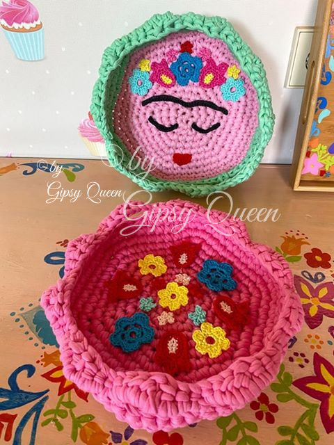 Zwei gehäkelte Utensilos in Pink: flaches Körbchen mit Blumenapplikationen und rundes Utensilo mit Gesichtsmotiv und grünem Rand
