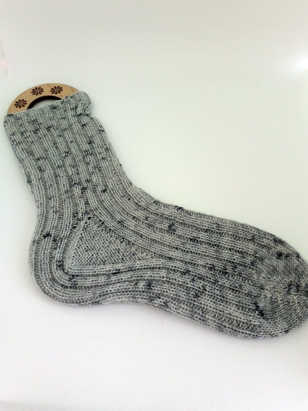 Light-grey ribbed sock on wooden blocker showing heel flap, turned heel and toe shaping