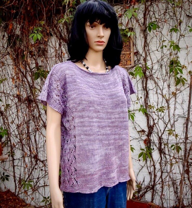 Schaufenstermannequin trägt lila gestricktes Kurzarm-Shirt mit Ajourmuster an den Seiten vor einer efeubewachsenen Wand