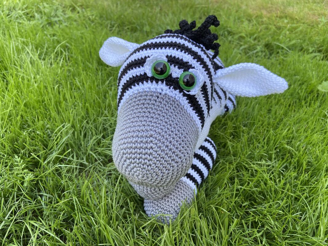 Nahaufnahme eines gestreiften Zebra-Amigurumi mit grauer Schnauze und grünen Sicherheitsaugen