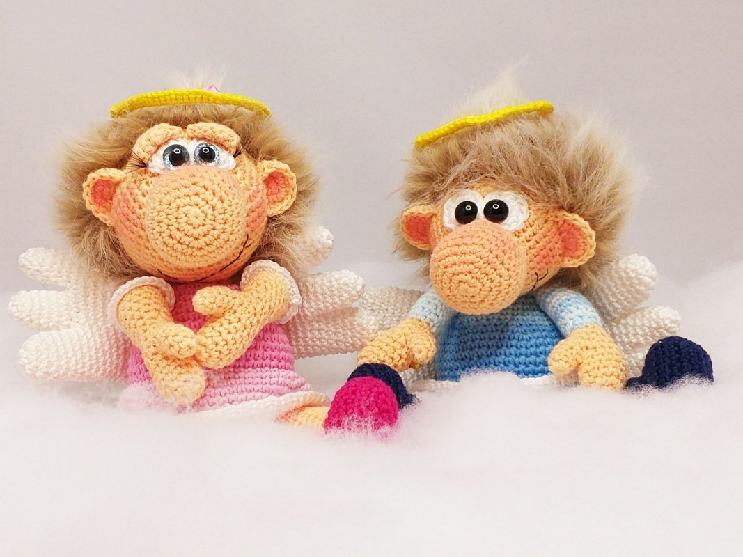 Two crochet amigurumi angel dolls with yellow halos, white wings, fluffy hair, and pink and blue outfits on a white background