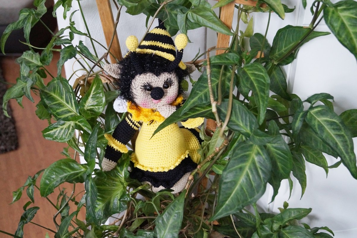 Gehäkeltes Bienen-Amigurumi mit gelb-schwarzem Kostüm zwischen Pflanzenblättern
