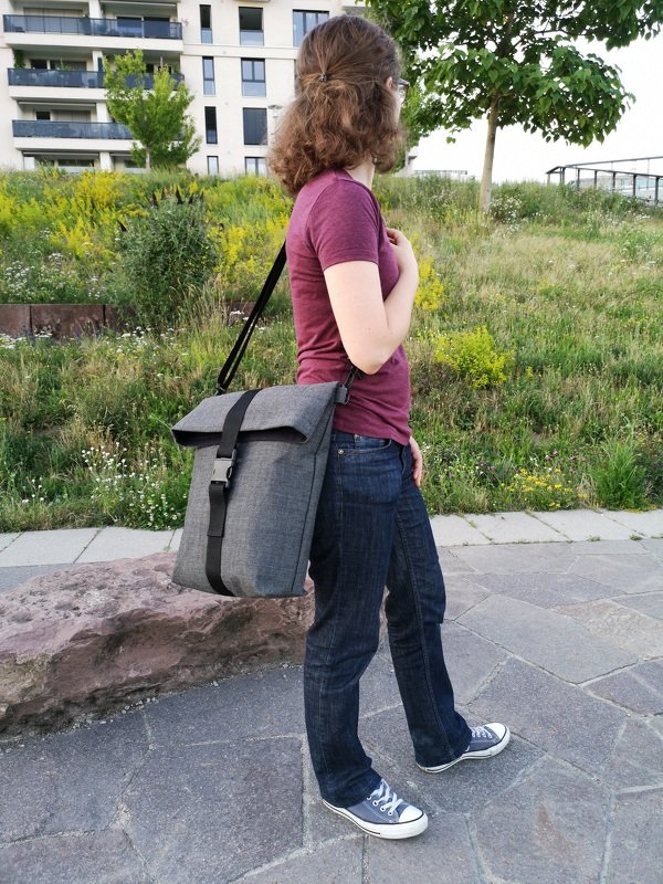 Graue Rolltop-Umhängetasche mit verstellbarem Trageriemen an einer Person