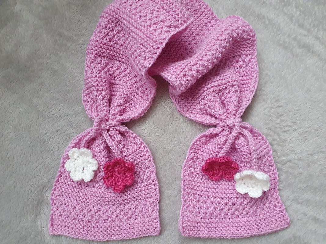 Rosa gestrickter Kinderschal mit zwei Täschchen und weißen sowie dunkelrosa Häkelblüten