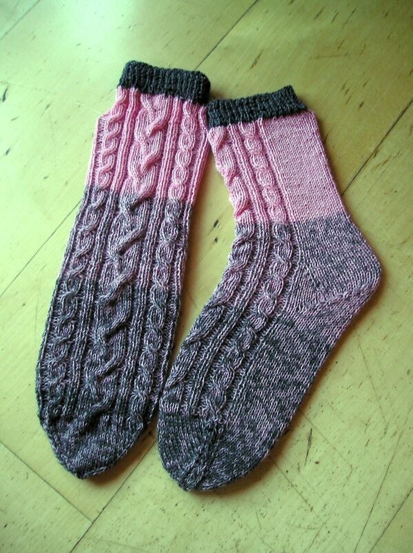Gestrickte Damensocken rosa-grau mit Zopfmuster auf Holzboden