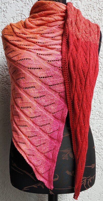 Gestricktes Tuch in Orange-, Rosa- und Rottönen mit wellenförmigem Lochmuster, drapiert auf einer Schaufensterpuppe.