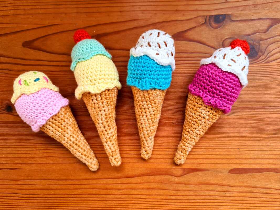 Vier gehäkelte Eiswaffeln in verschiedenen Farben auf Holzuntergrund