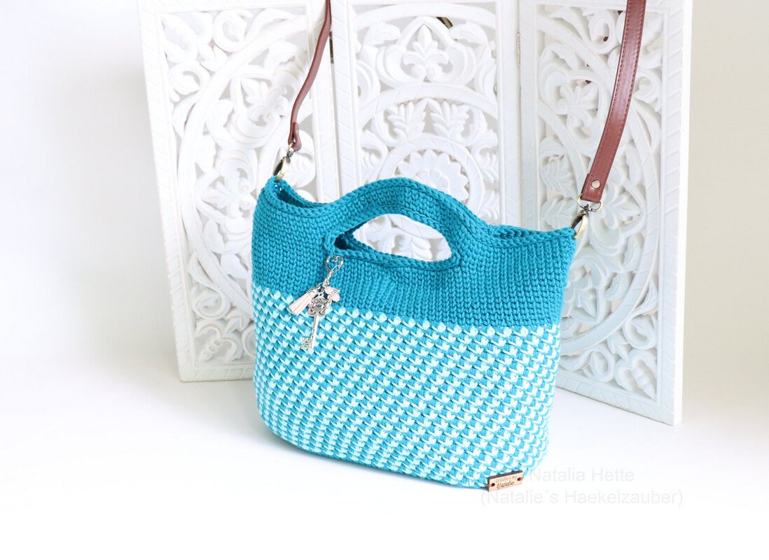Teal and white two-tone crocheted handle bag with cut-out handles, removable brown shoulder strap, and key-and-tassel charm.