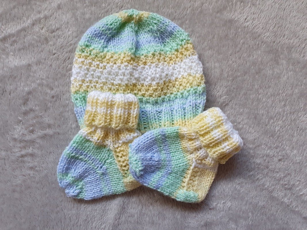 Gestricktes Babyset mit gestreifter Mütze und zwei passenden Schühchen in Pastellfarben auf hellem Hintergrund.