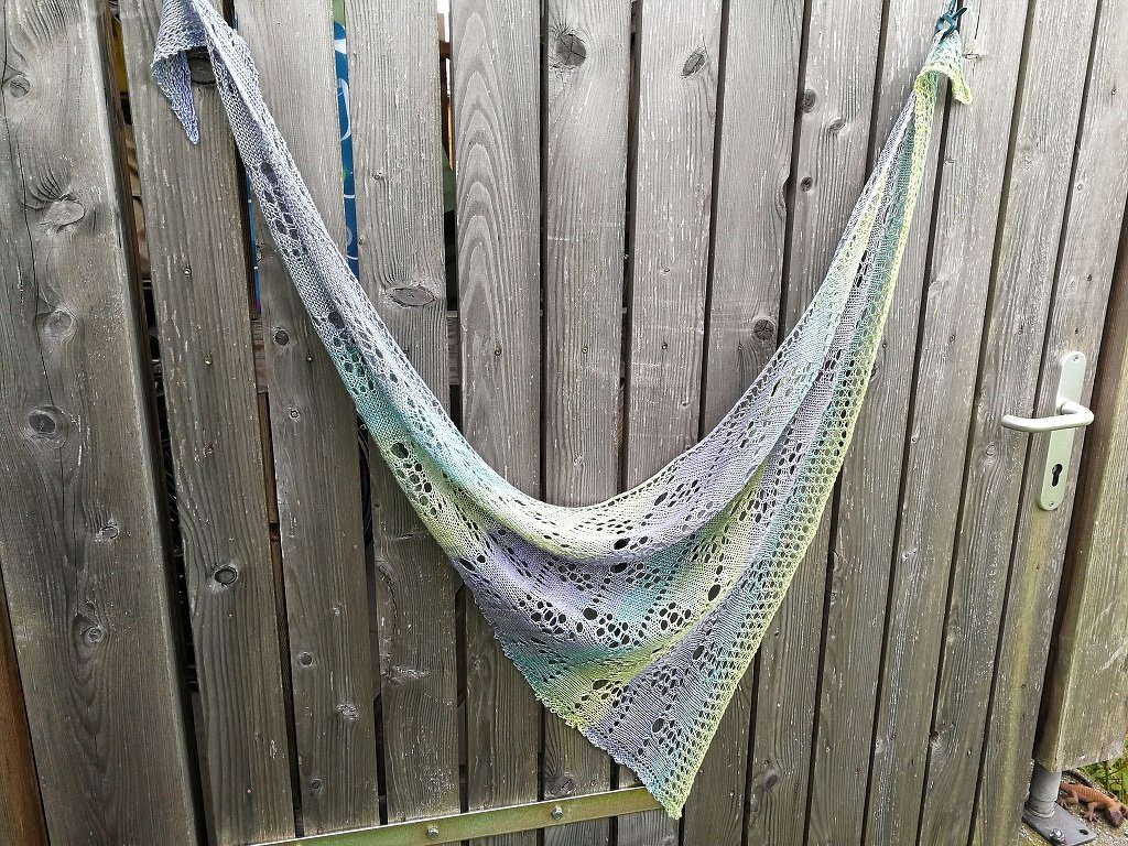 Gestricktes Dreieckstuch in Blau, Lila, Türkis und Hellgrün mit Lochmuster, an einem Holztor hängend