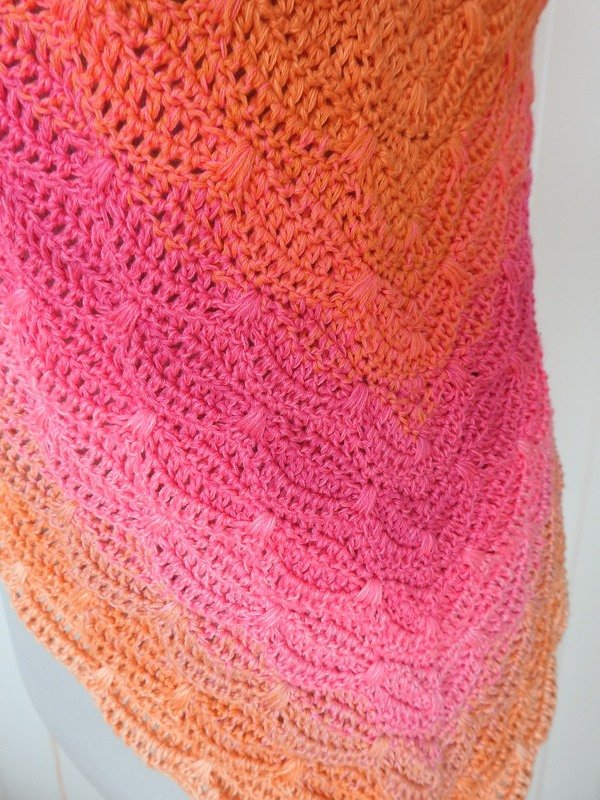 Close-up of a triangle crochet shawl with pink-to-orange gradient and chevron texture