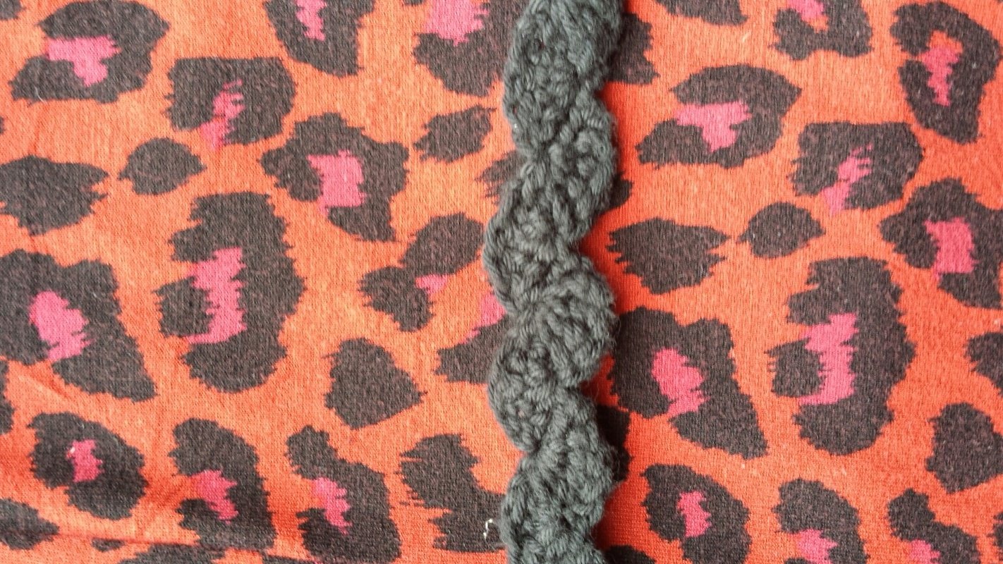 Dunkelgraue, schnell gehäkelte Wellenborte auf orangefarbenem Leopardenstoff