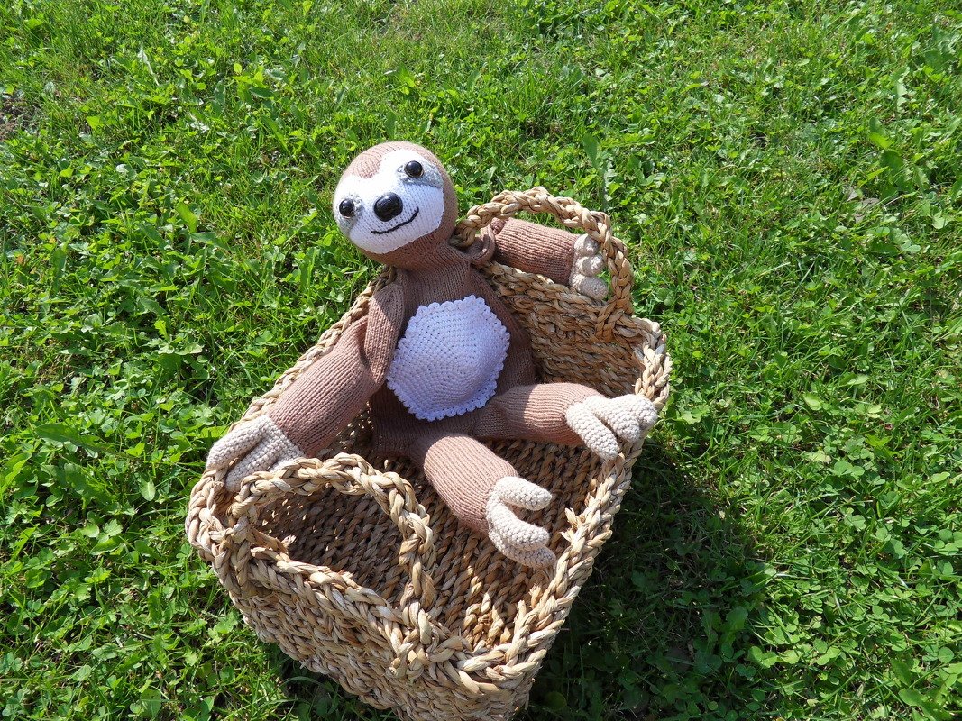 Handgestricktes Faultier-Stofftier in Weidenkorb auf grüner Wiese