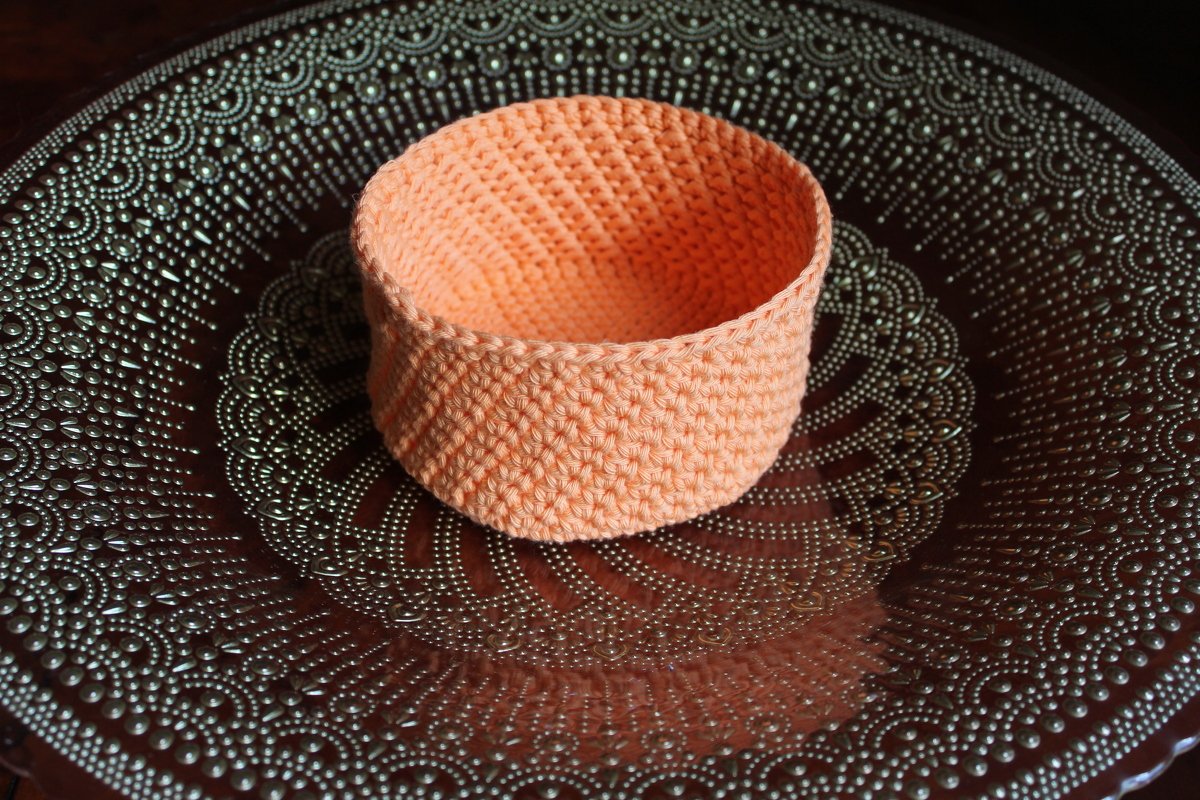 Gehäkelter runder Korb in Pfirsichfarbe auf einem gemusterten Tablett