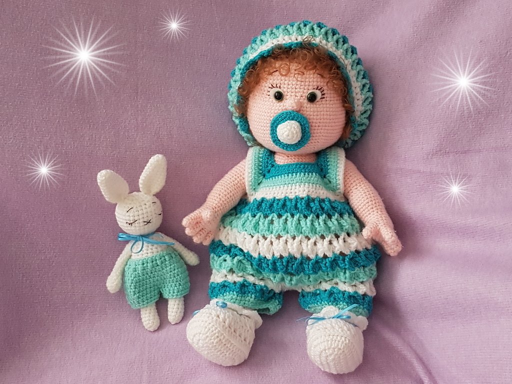 Gehäkelte Amigurumi-Babypuppe mit braunem Lockenkopf, Schnuller und kleinem gehäkelten Hasen auf lila Untergrund.