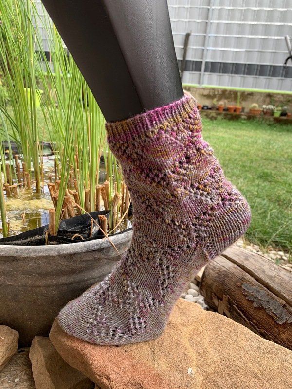 Gestrickte Kurzsocke in rosé-lila Melierung mit Ajourmuster an einem Schaufensterbein