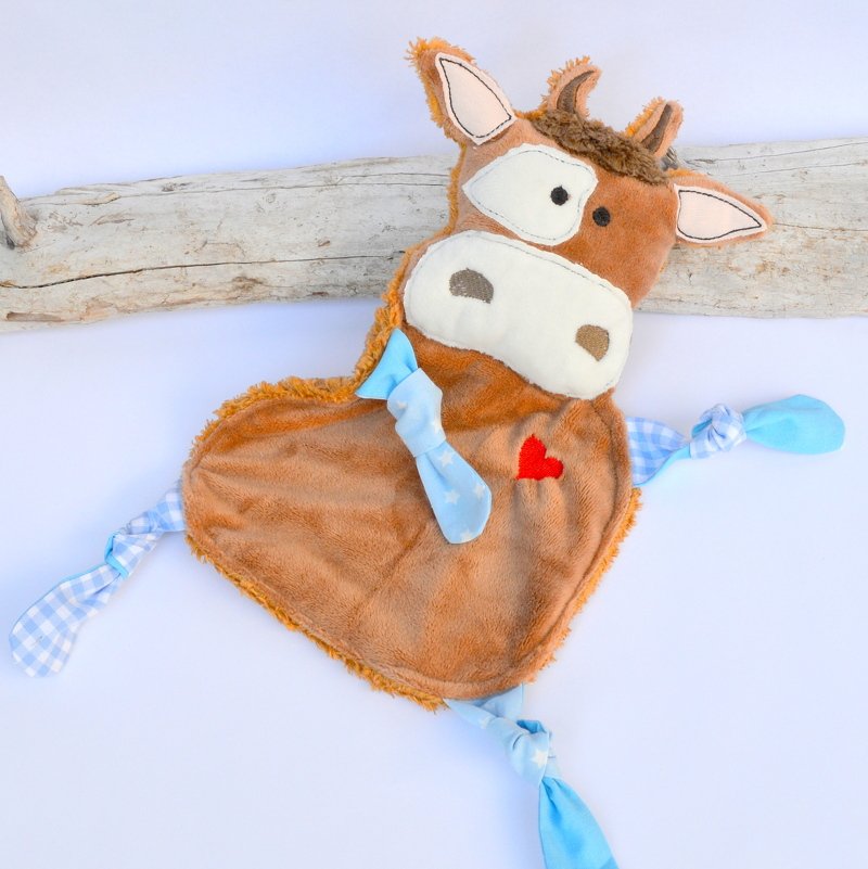 Braunes Kuscheltuch in Kuhform mit rotem Herz und blauen Knoten auf hellem Hintergrund.