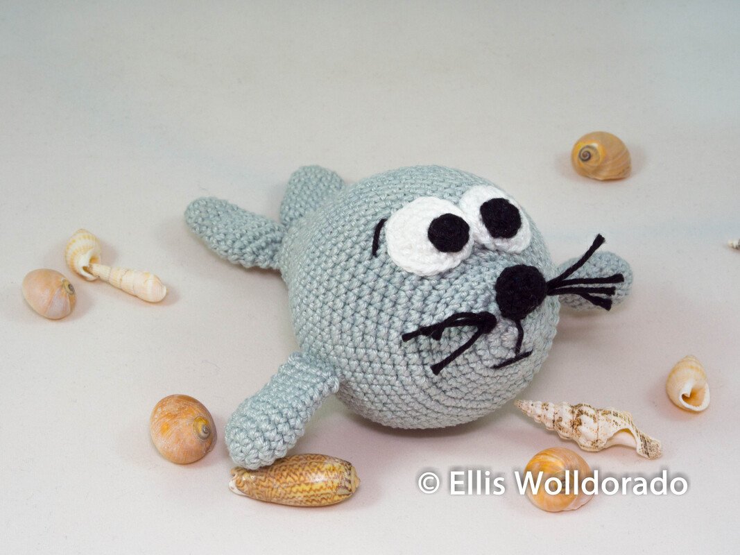 Hellgraue gehäkelte Amigurumi-Robbe mit großen Augen und Muscheln