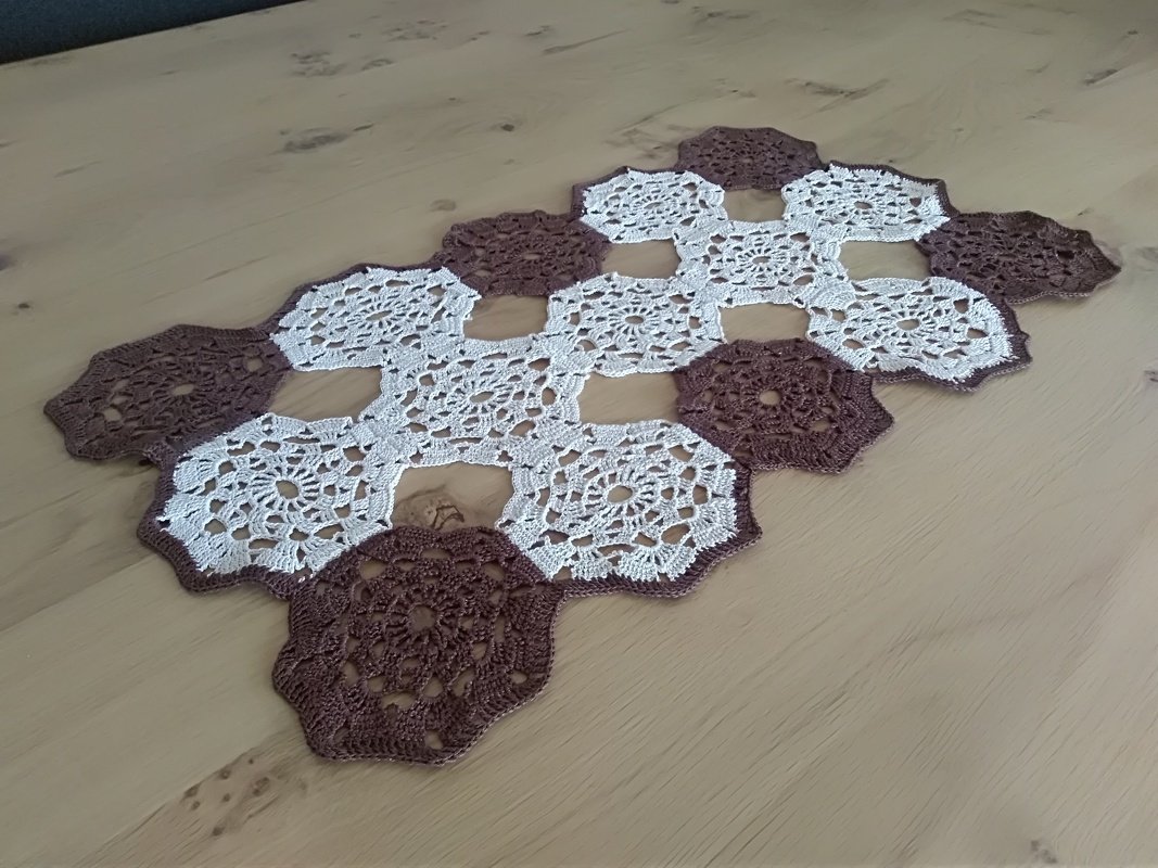 Gehäkelter Tischläufer aus Sechsecken in Creme und Braun auf hellem Holztisch