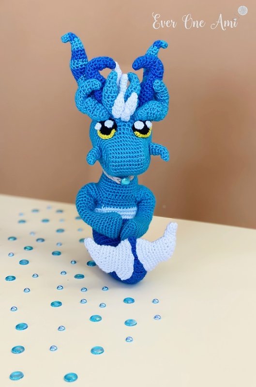 Gehäkelter blauer Amigurumi-Drache mit gedrehten Hörnern und gelb-schwarzen Augen