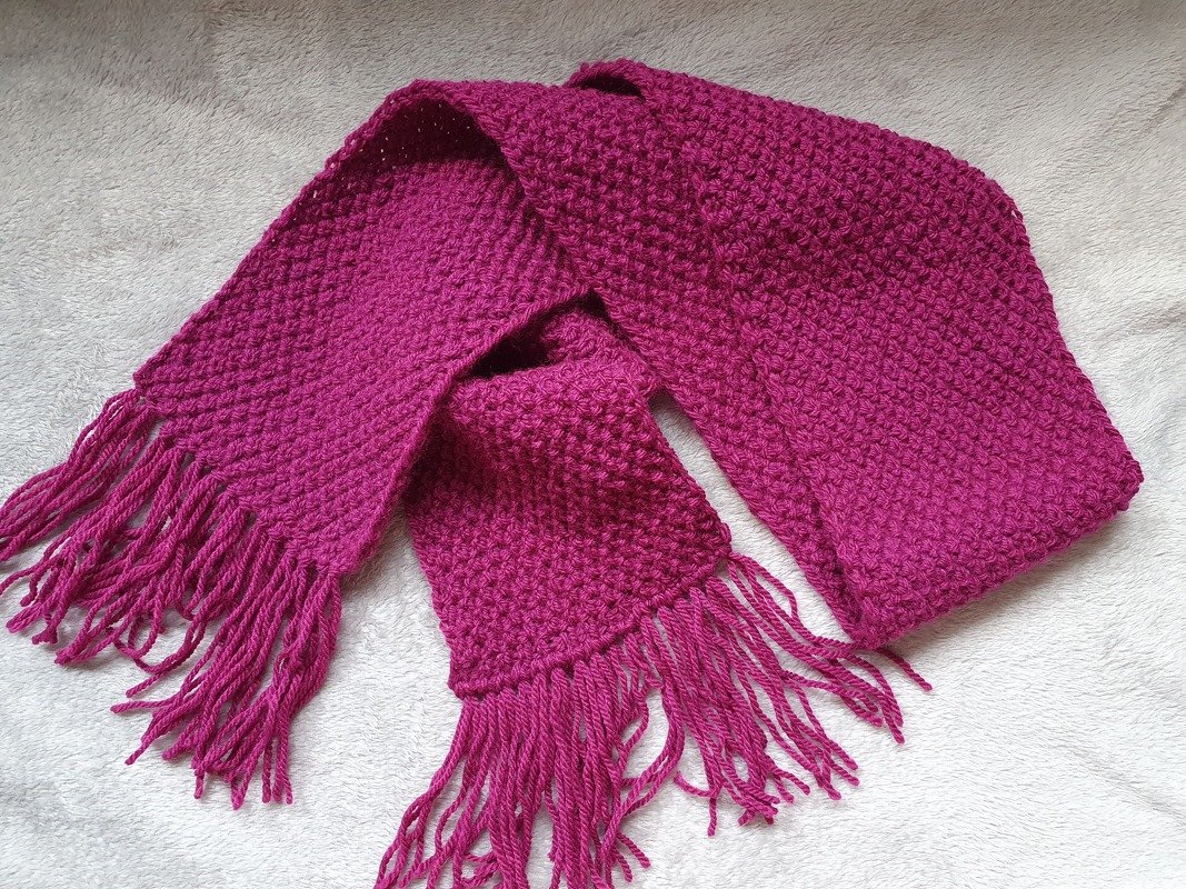 Gestrickter fuchsiafarbener Kinderschal mit Fransen auf hellem Untergrund
