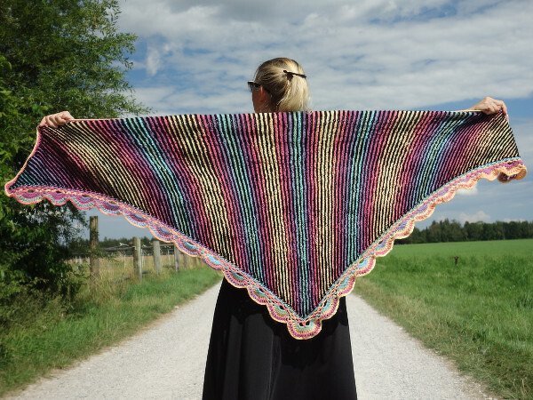 Person hält großes gestricktes Dreieckstuch mit bunten Streifen und Muschelkante ausgebreitet