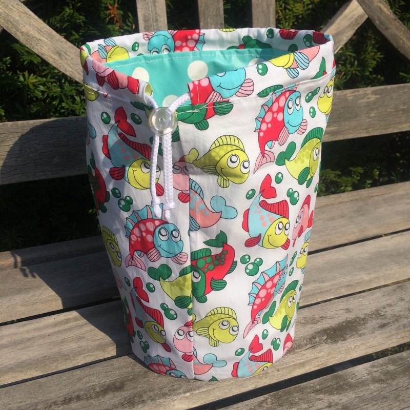 Stofftasche mit farbenfrohem Fischmotiv und Kordelzug auf Holzbank.