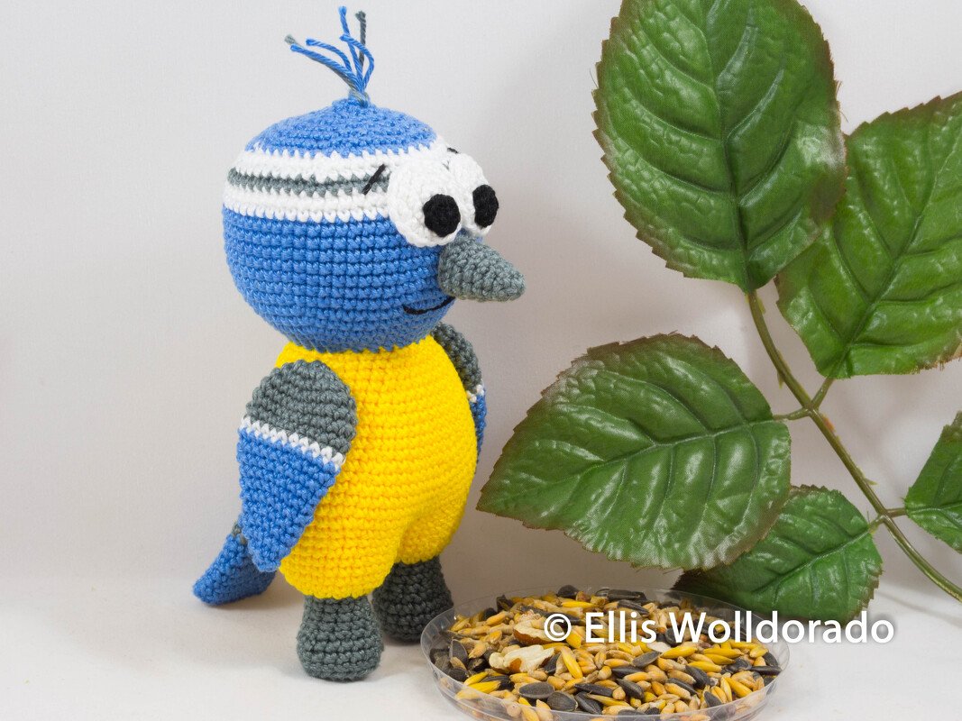 Gehäkelter Amigurumi-Vogel blau gelb mit grauem Schnabel neben Futterschale