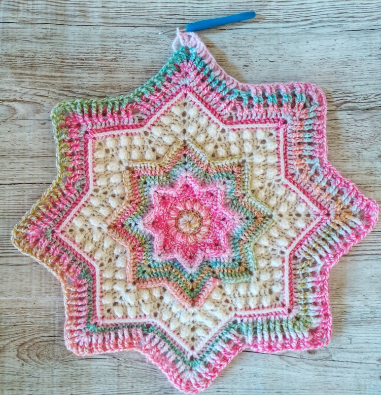 Work-in-progress star crochet motif with crochet hook on wooden background