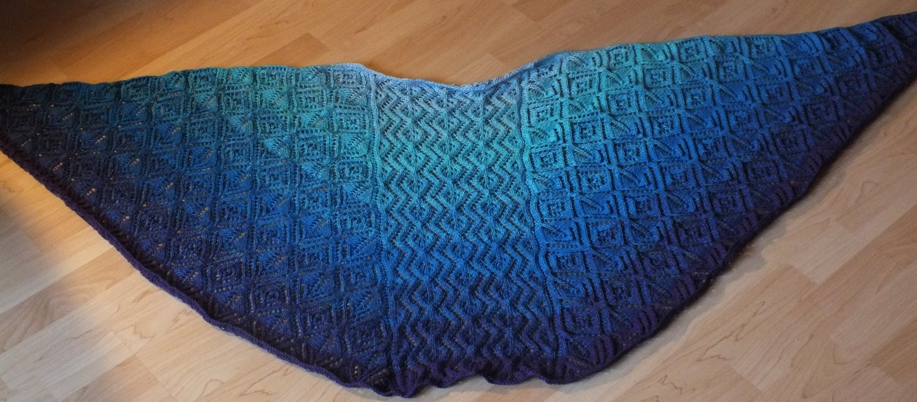 Gestricktes Dreieckstuch mit Verlaufsgarn von grün zu blau bis violett, mittigem Reliefmuster und seitlichen geometrischen Kästchen