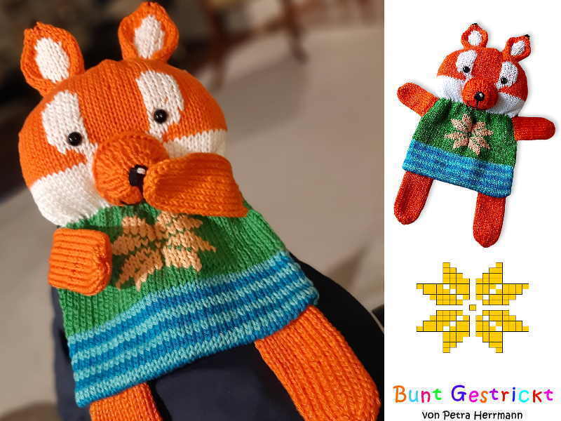 Orange and white knitted fox baby puppet wearing a green and blue striped sweater with a star motif